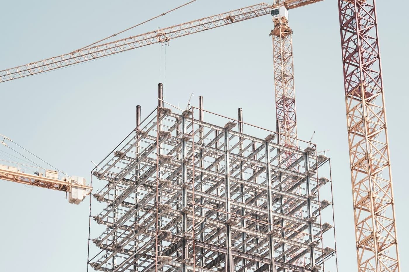 A steel building frame rising between tower cranes