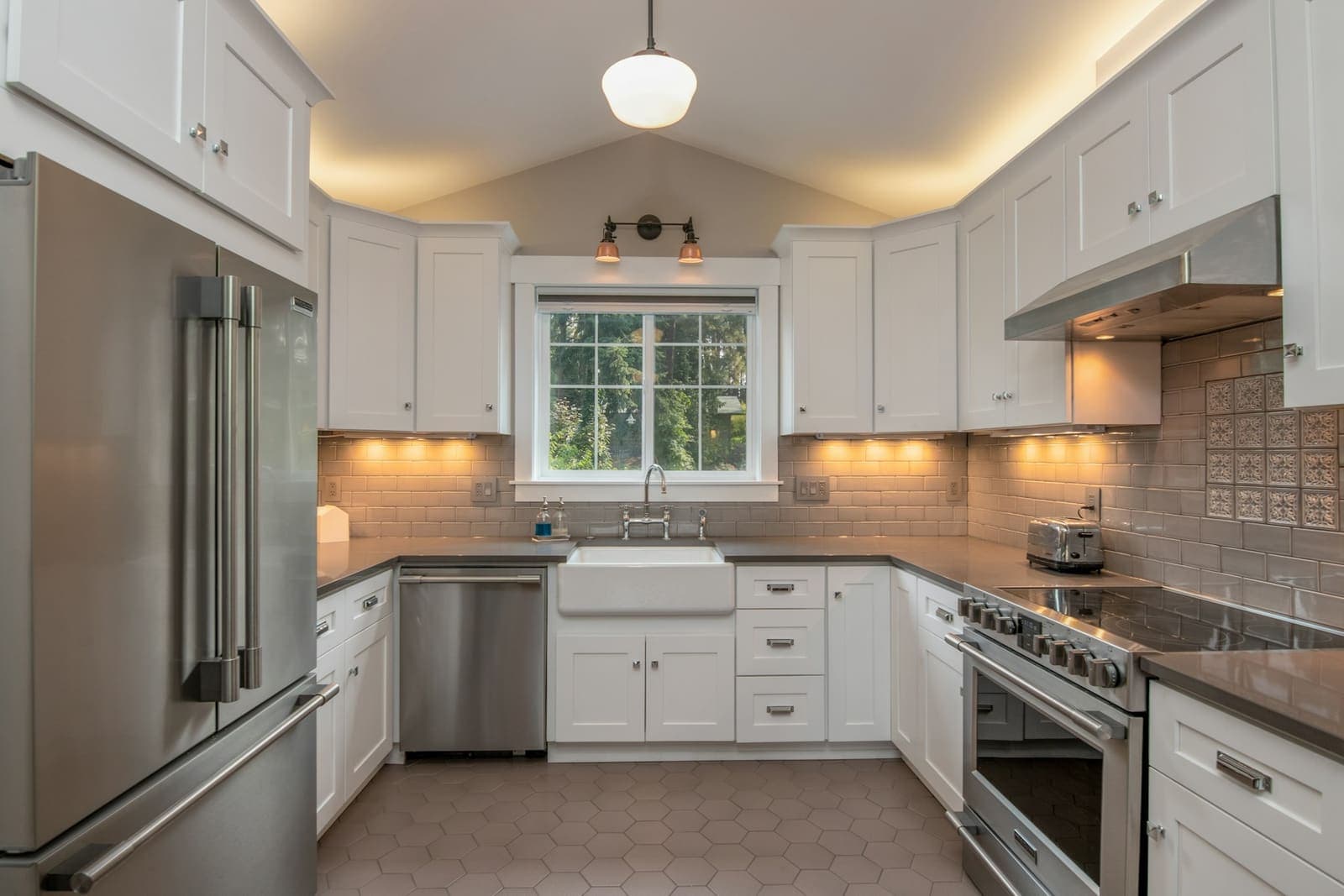 A finished kitchen with white shaker cabinets and a pendant light